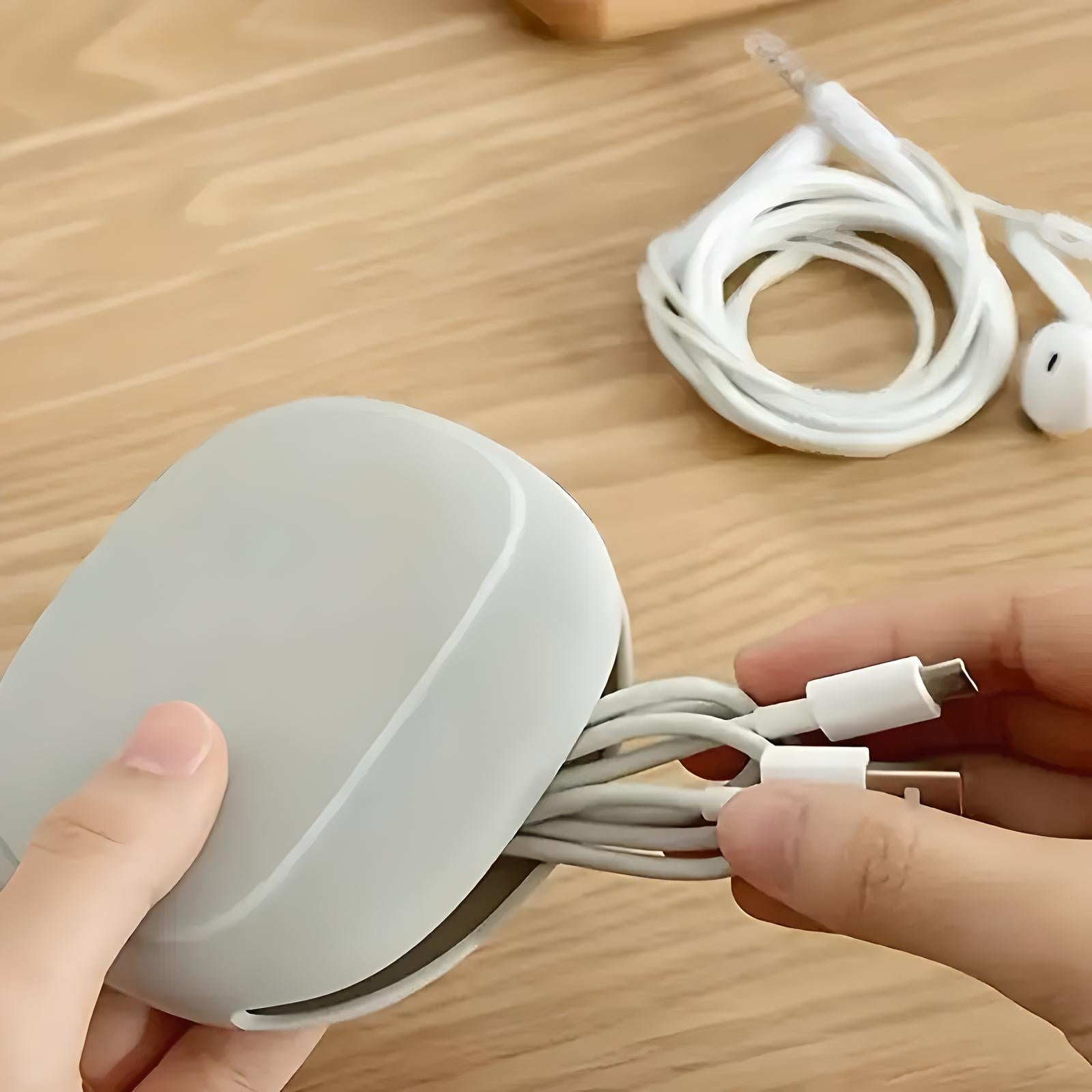 Person organizing white USB-C cables into a compact, gray cable organizer on a wooden table; efficient cable management solution.