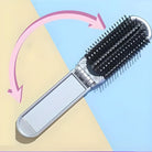 Folding hairbrush with black bristles and silver handle on a pastel background, featuring a pink arrow indicating its compact, portable design.