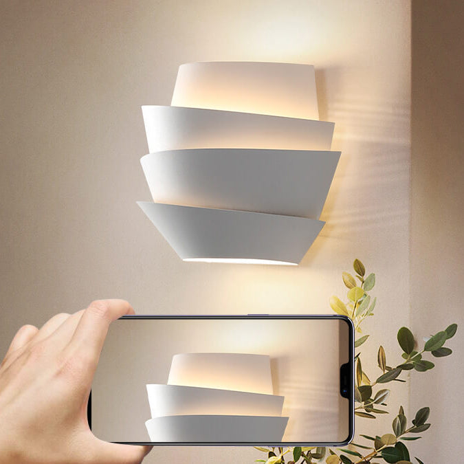 Modern white LED wall sconce with layered geometric design, illuminating a room. Energy-efficient lighting fixture, contemporary home decor.