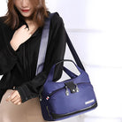 Woman holding a stylish blue nylon shoulder bag with multiple zippered compartments, ideal for travel and daily use. Fashionable and functional accessory.