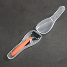 Orange razor in a transparent travel case on a dark background, featuring a sleek design and protective cover. Ideal for travel grooming essentials.