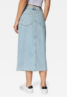 Woman wearing a light blue denim midi skirt with frayed hem, paired with white sneakers and a white top. Fashionable casual outfit for women.