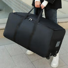 Large black travel duffel bag with wheels and handles, carried by a person in casual attire. Ideal for luggage, travel, and storage solutions.