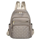 Stylish taupe backpack with quilted front pocket, gold zippers, and adjustable straps. Perfect for travel, school, or daily use. Fashionable and functional.