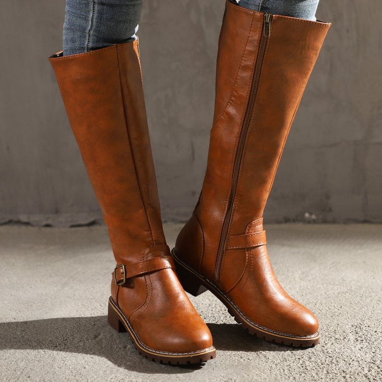 Brown leather knee-high boots with buckle detail and side zipper, worn with jeans. Stylish women's footwear, perfect for fall fashion.