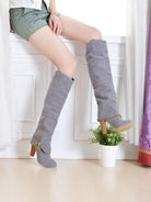 Woman wearing stylish gray knee-high boots with wooden heels, sitting on a windowsill. Fashionable footwear, trendy fall boots, chic style.