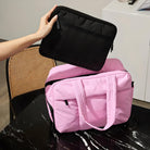 Person placing a black laptop sleeve into a pink travel duffel bag on a marble table. Stylish, functional luggage for travel and work essentials.