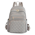 Stylish gray backpack with quilted front pocket, gold zippers, and multiple compartments. Perfect for travel, school, or daily use. Fashionable and functional.