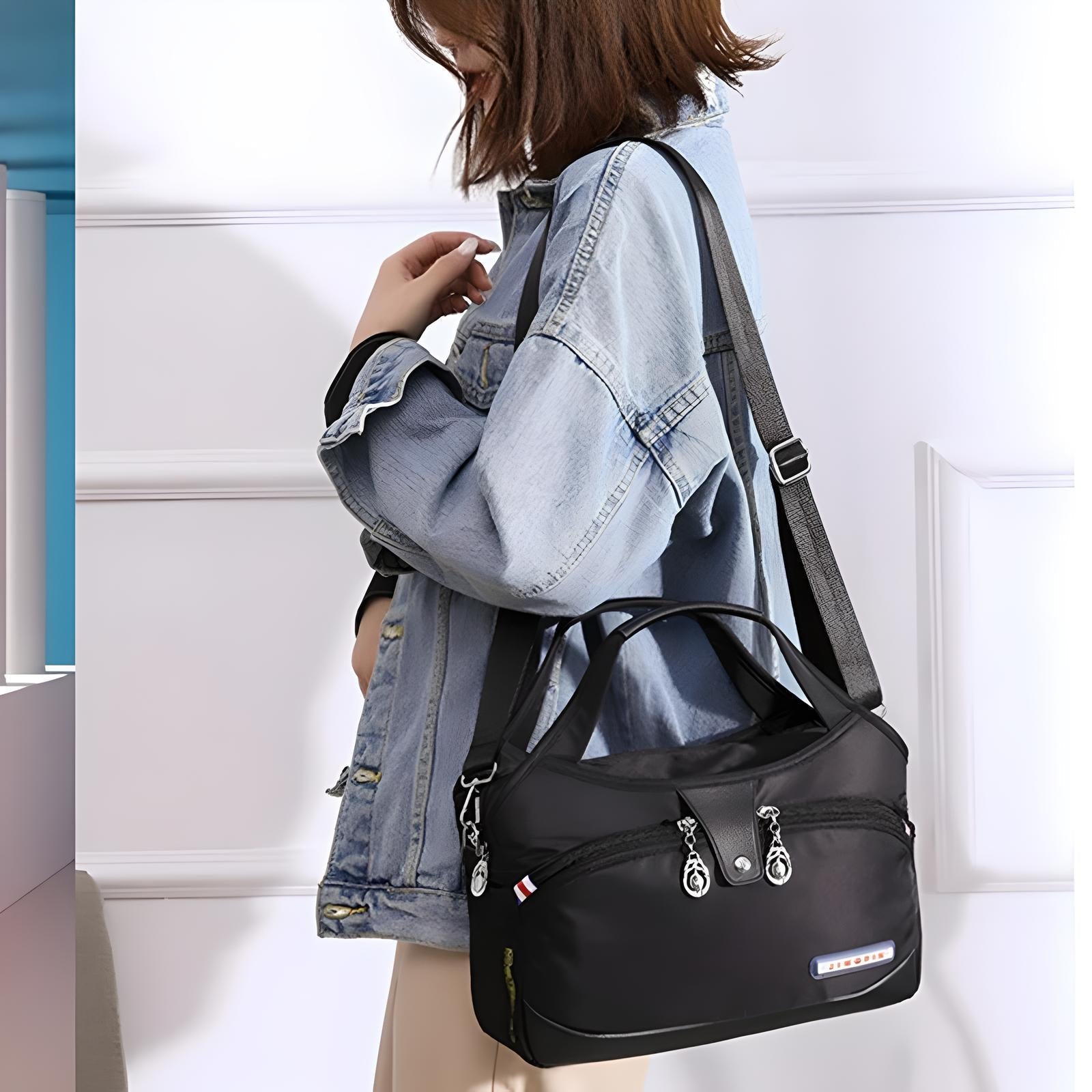 Woman wearing denim jacket carrying a stylish black crossbody bag with multiple zippers and adjustable strap, perfect for travel and daily use.