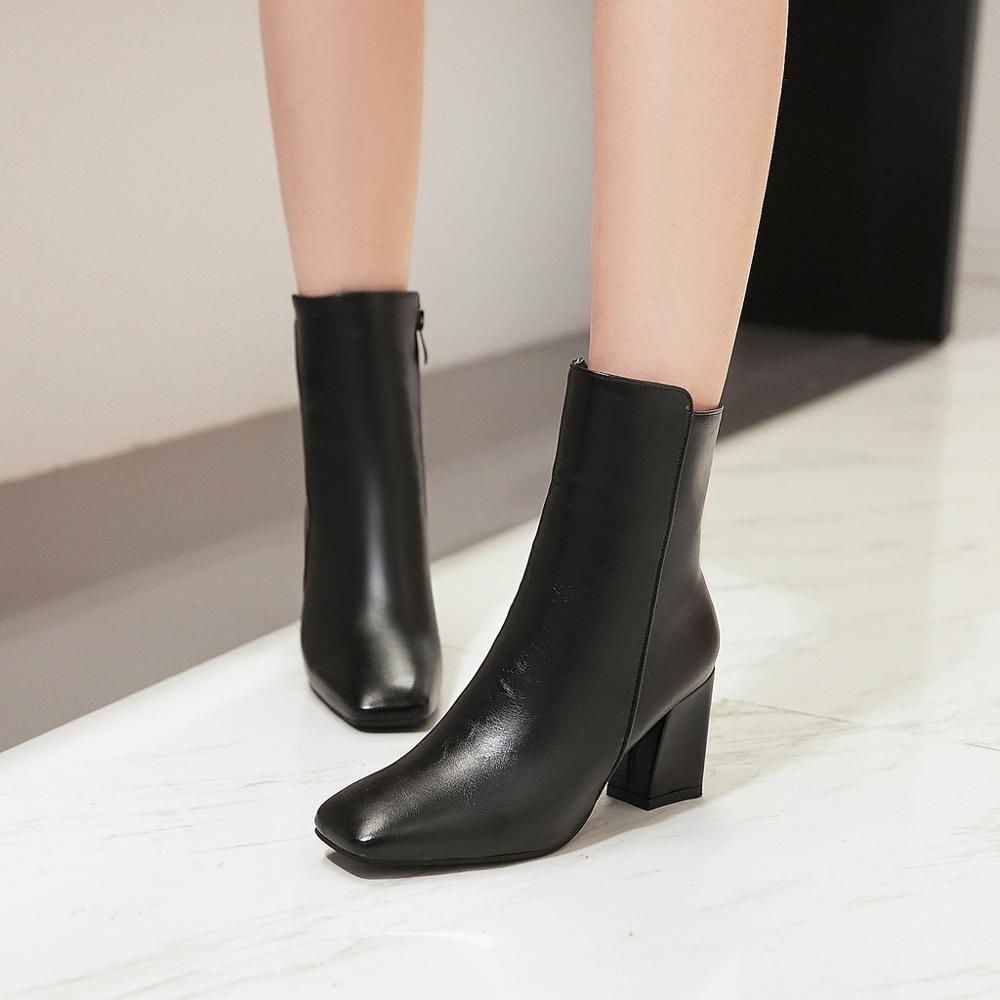 Black leather ankle boots with block heels on a marble floor, showcasing sleek design and modern fashion footwear for women.