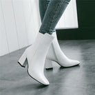 White ankle boots with block heels and pointed toes, worn with skinny jeans on a tiled floor. Fashionable women's footwear, stylish and modern design.