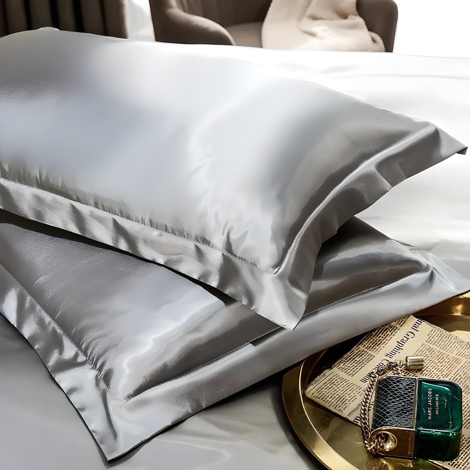 Luxurious silver silk pillowcases on a bed, accompanied by a gold tray with a newspaper and perfume bottle. Elegant bedroom decor, soft bedding.