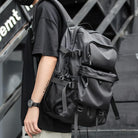 Man wearing a black tactical backpack with multiple compartments and mesh pockets, ideal for urban travel and outdoor adventures. Stylish and functional design.