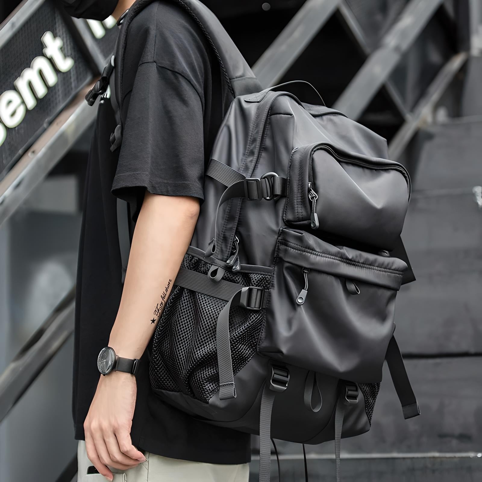 Man wearing a black tactical backpack with multiple compartments and mesh pockets, ideal for urban travel and outdoor adventures. Stylish and functional design.