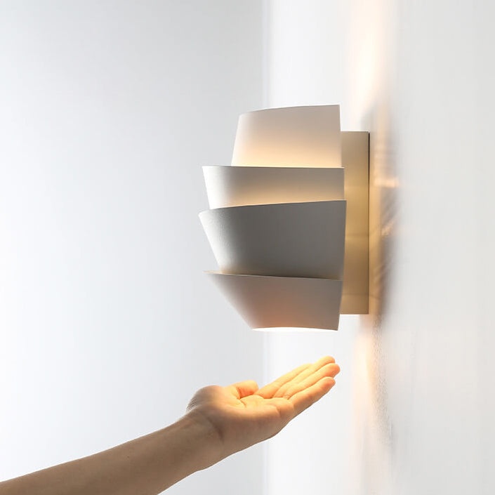 Modern white wall sconce with layered design, illuminating a hand beneath. Contemporary lighting fixture, minimalist home decor, soft ambient light.