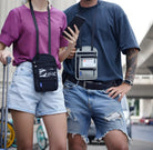 Two people wearing casual outfits with crossbody phone pouches; one black, one gray. Keywords: crossbody phone pouch, casual fashion, travel accessories.