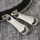 Close-up of dual silver zipper pulls on a textured gray fabric bag, highlighting durable metal design and stylish accessory detail.