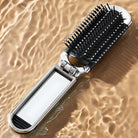 Silver hairbrush with black bristles and mirror handle on rippled water surface, reflecting light. Stylish, multifunctional grooming tool.