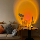 Cozy living room with ambient sunset lamp casting warm orange glow on wall, illuminating wine glasses and decorative vases on a side table.