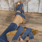 Blue strappy sandals with woven design on a wooden floor, worn with ripped jeans. Comfortable summer footwear, casual style, women's fashion.