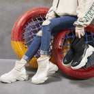 Trendy sock sneakers with chunky soles in black and white, styled with ripped jeans, against a colorful tire backdrop. Fashionable footwear for casual wear.