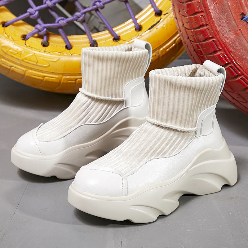 Chunky white platform sneakers with ribbed sock-like upper, set against colorful tire backdrop. Trendy footwear for fashion-forward street style.