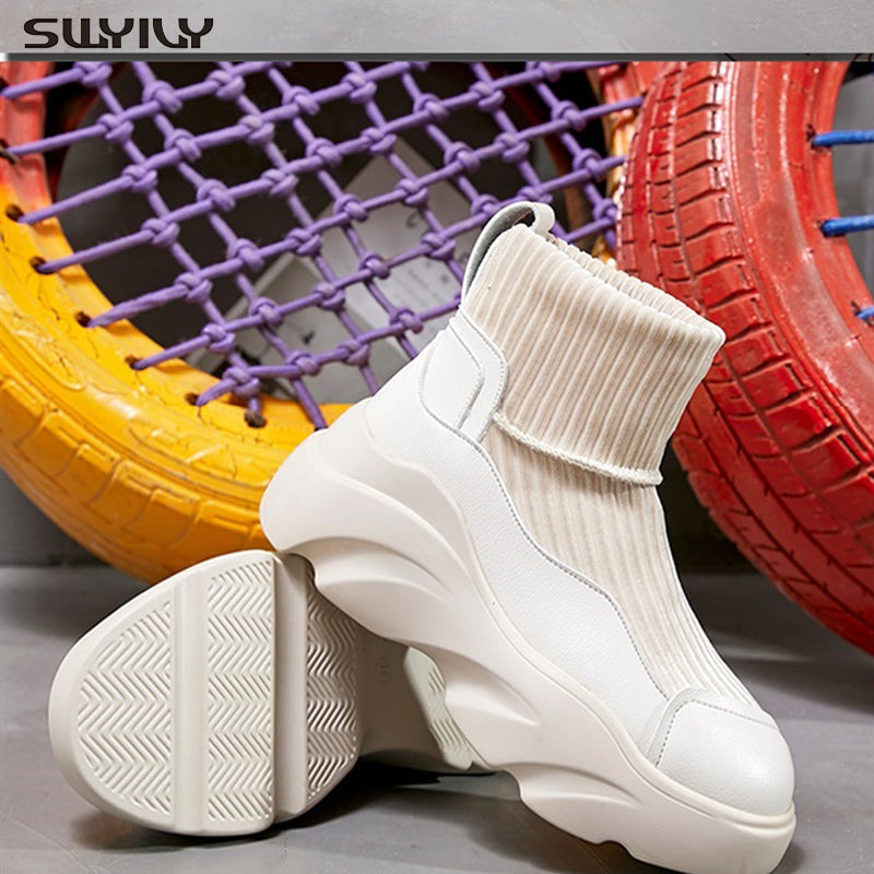 Trendy white sock sneakers with chunky soles, featuring ribbed knit design, displayed against colorful tire backdrop. Fashionable footwear for casual wear.