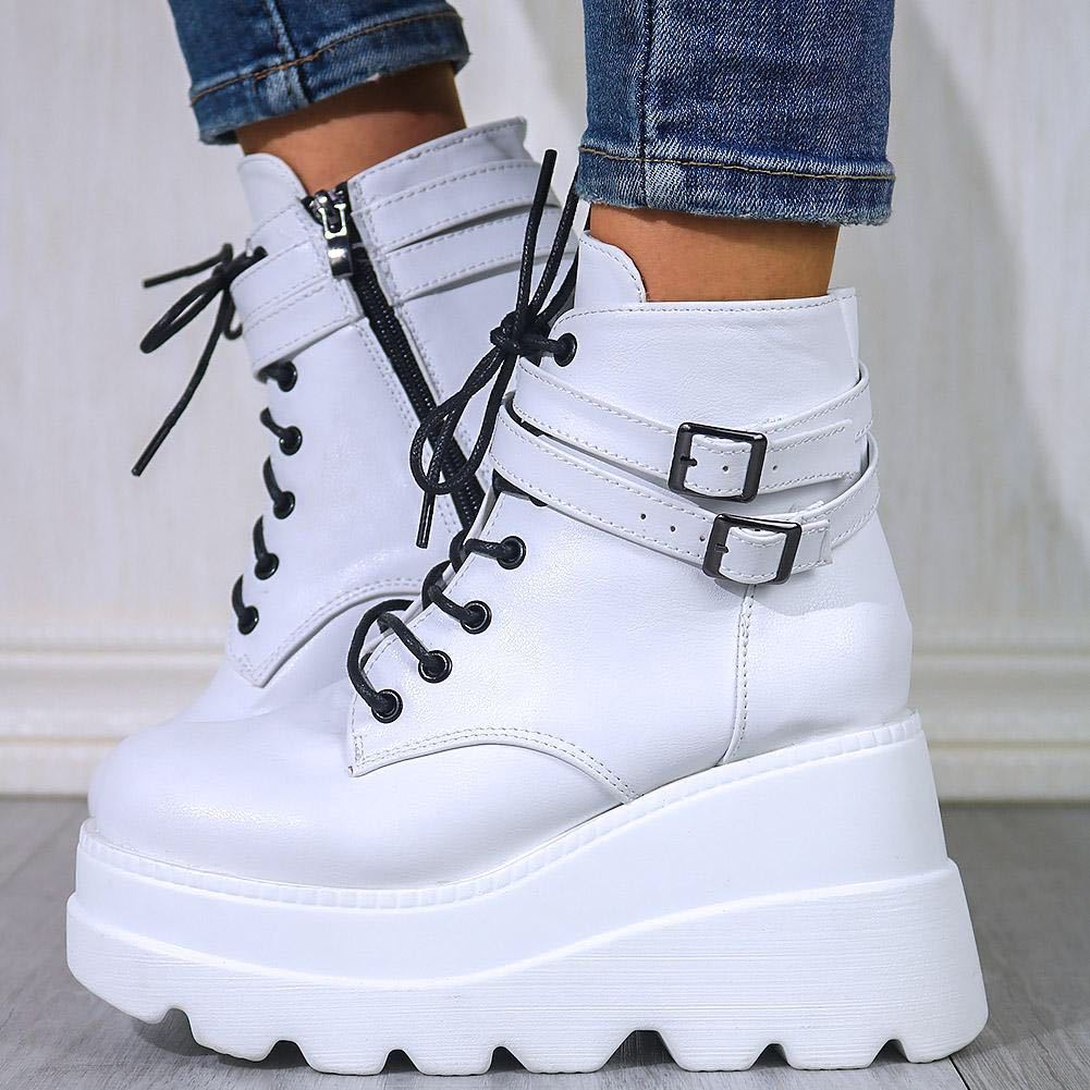 White platform ankle boots with black laces and side zippers, featuring chunky soles and buckle straps, paired with blue jeans. Fashion footwear.