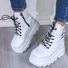 White platform ankle boots with black laces and side zippers, worn with blue jeans on a wooden floor. Fashionable women's footwear.