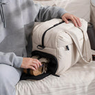 Person packing shoes into a beige travel duffel bag with multiple compartments, ideal for organized travel and storage.