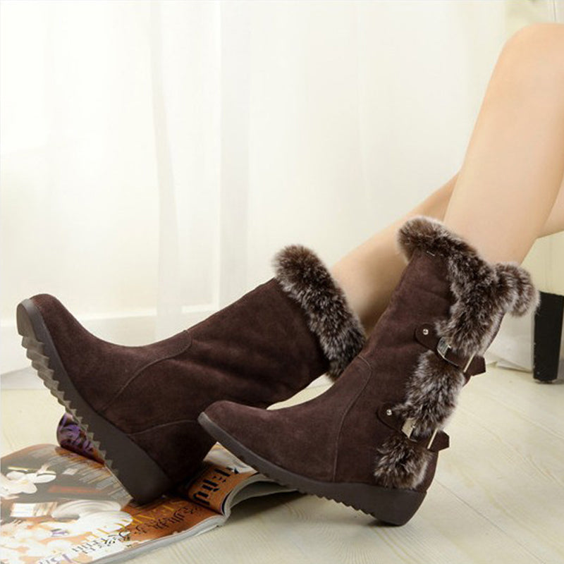 Brown suede winter boots with faux fur trim and buckle accents, perfect for cold weather fashion. Stylish women's footwear on a light wooden floor.