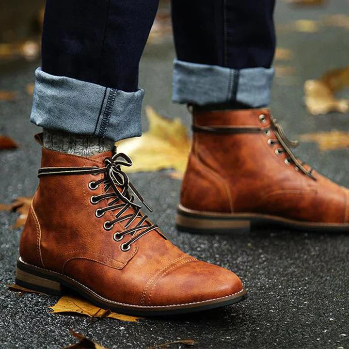 Brown leather lace-up boots on wet pavement with fallen autumn leaves; stylish men's footwear, casual fashion, outdoor fall style.