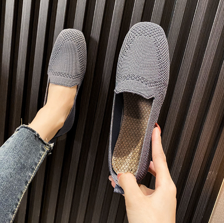 Gray woven slip-on loafers with textured design, held in hand against a striped background. Comfortable, stylish footwear for casual wear.