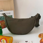 Olive green crescent shoulder bag on a table with Matisse book, orange juice, and bread. Stylish, minimalist accessory for casual fashion.