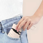 Hand placing compact beige leather wallet with strap into blue jeans pocket, showcasing minimalist design and convenient portability.