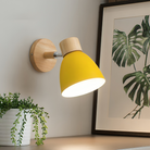 Yellow wall-mounted lamp with wooden accents illuminating a modern interior, next to a framed botanical print and a potted plant on a shelf.