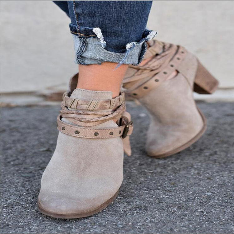 Beige suede ankle boots with braided straps and studded details, paired with rolled-up denim jeans. Fashionable women's footwear on pavement.