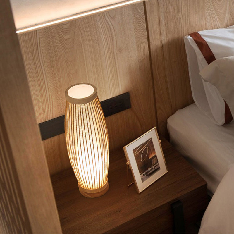 Modern wooden bedside lamp with warm light on a nightstand, next to a framed photo, in a cozy bedroom setting. Ideal for home decor and lighting.