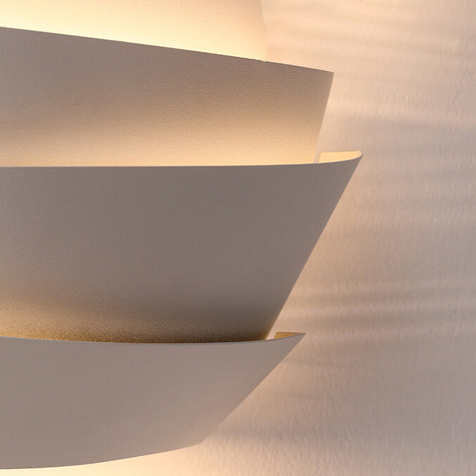 Modern white wall sconce with layered design, emitting soft ambient light. Contemporary home lighting fixture, minimalist decor, interior design.