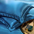 Luxurious blue silk pillowcases on a bed, accompanied by a gold tray with perfume and accessories. Elegant bedroom decor, premium bedding.