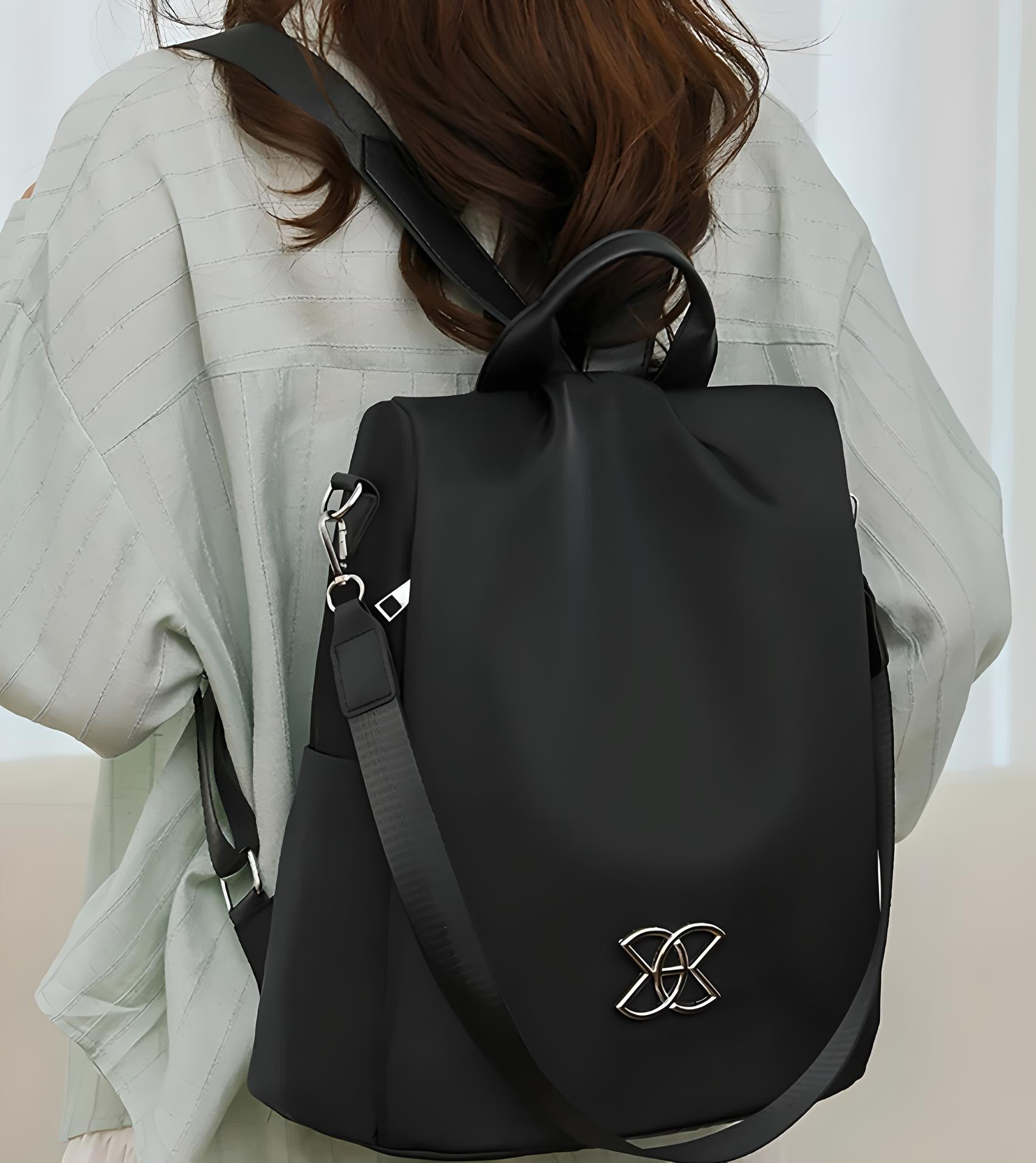 Stylish black leather backpack with silver buckle, worn by a woman in a light blouse. Perfect for fashion-forward travel and daily use.