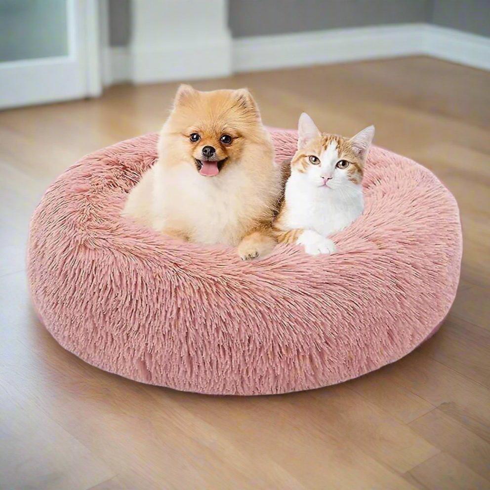 Pomeranian dog and tabby cat cuddling in a plush pink pet bed on wooden floor, cozy home decor, pet comfort, fluffy pet bed for dogs and cats.