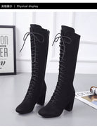 Black knee-high lace-up boots with block heels on a gray surface, featuring a sleek design ideal for fashion-forward footwear enthusiasts.