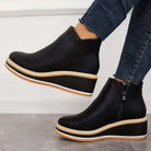 Black wedge ankle boots with side zipper, paired with dark denim jeans. Stylish women's footwear, perfect for casual and trendy outfits.