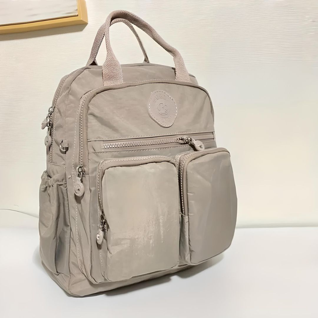 Beige backpack with multiple zippered pockets, durable fabric, and top handles. Ideal for travel, school, or work. Stylish and functional design.