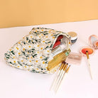 Floral makeup bag with daisy pattern, filled with cosmetics including brushes, lipstick, and compact powder on a beige background. Perfect for travel.