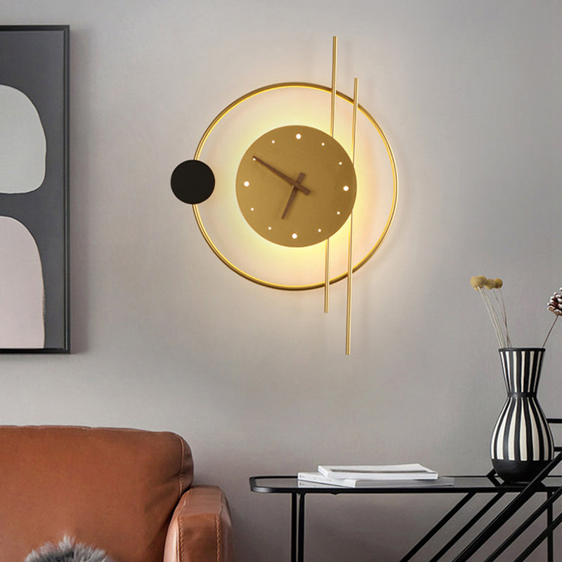 Modern geometric wall clock with gold accents and LED backlight, mounted on a gray wall above a black console table with a vase and books.