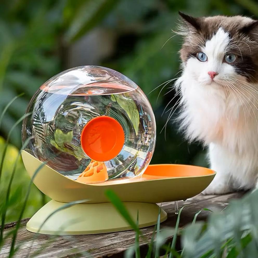 Cat drinking fountain with transparent globe design and orange accents, surrounded by greenery, ideal for pet hydration and modern home decor.