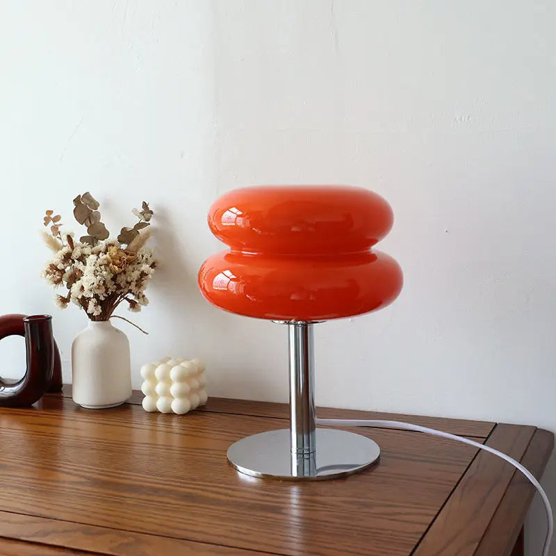 Retro orange glass table lamp with chrome base on wooden desk, minimalist home decor, modern lighting, next to white and brown vases with dried flowers.