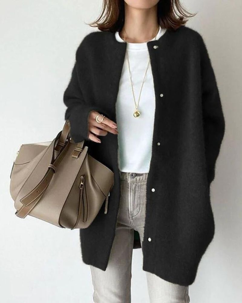 Woman wearing a black cardigan over a white shirt, holding a beige leather handbag. Fashionable casual outfit with gold necklace and rings.